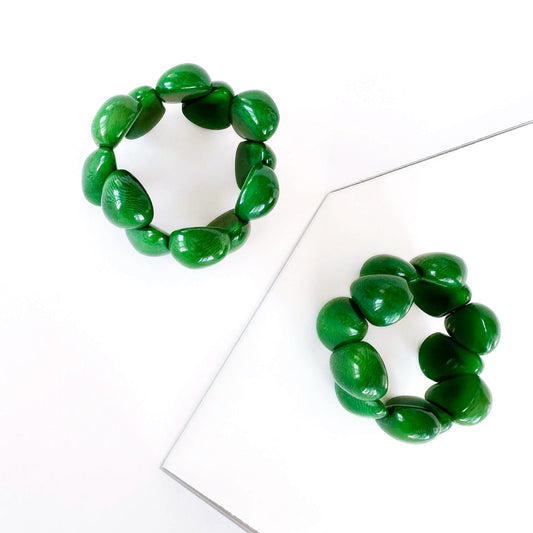A green tagua beaded stretch bracelet displayed on a clean white surface with a minimalist geometric mirror prop