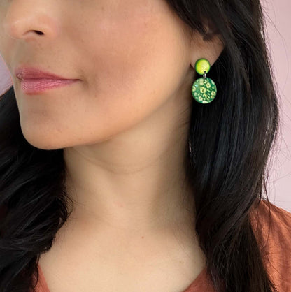 Close-up of a person wearing green tagua nut engraved earrings with a pink background