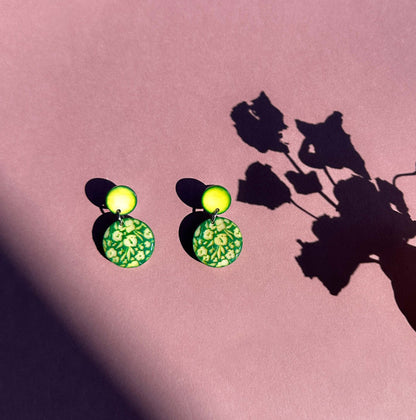 Green tagua nut earrings, engraved with a floral pattern on a pink background with floral shadows