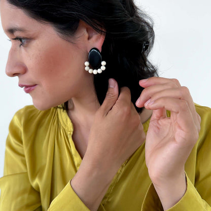 Woman wearing black earrings with white beads, handmade with tagua nut beads and natural dyes.