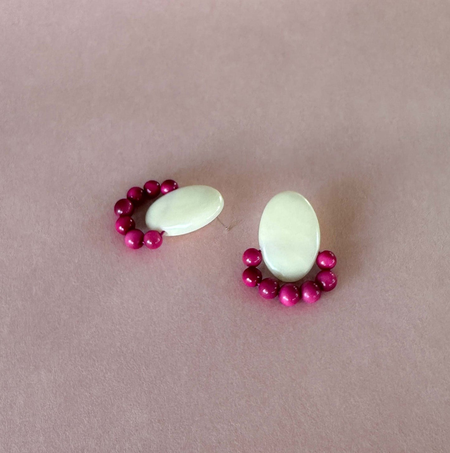 Pair of handmade earrings made with tagua nut beads and natural dyes on a pink background