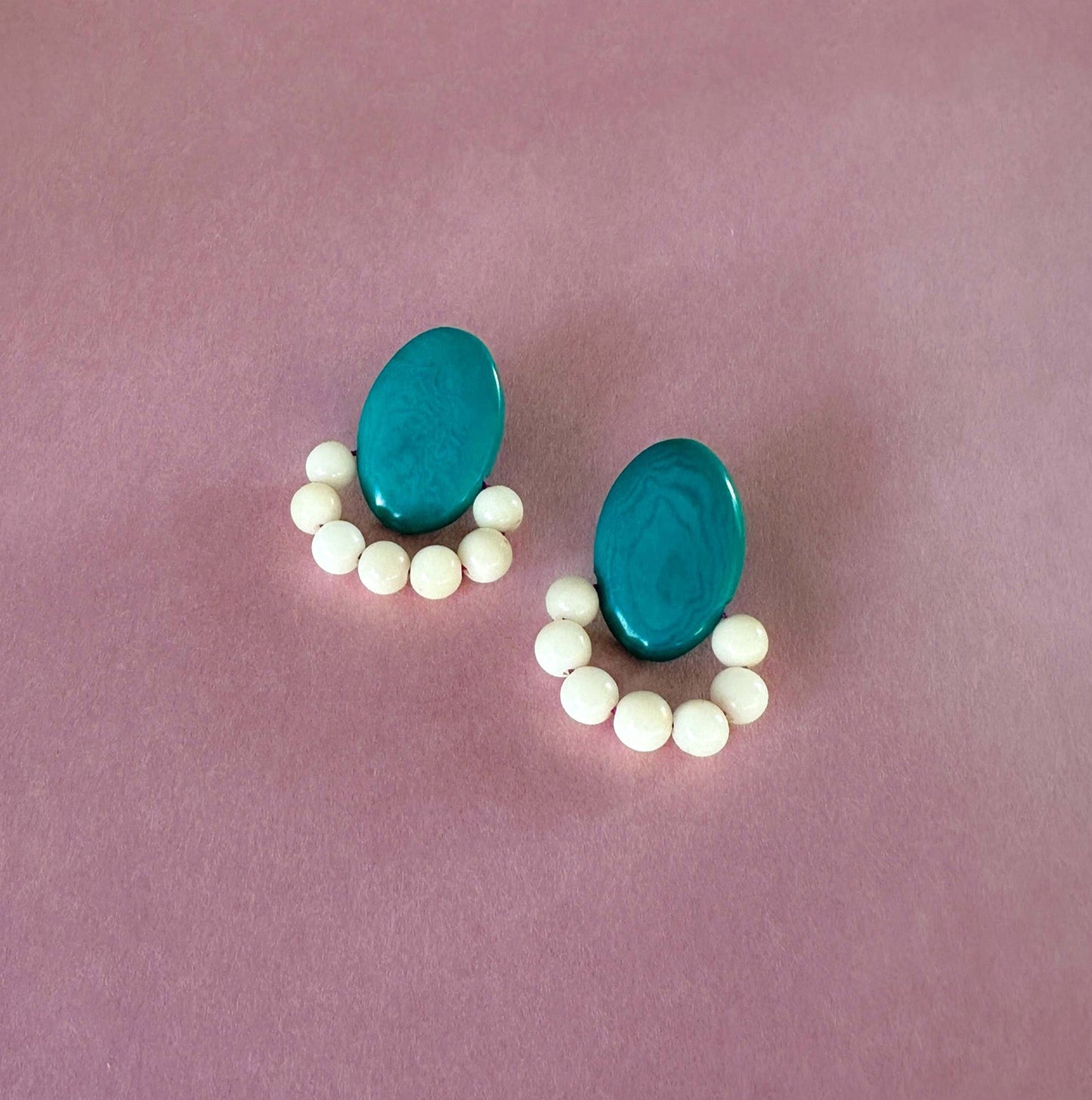 Teal earrings handmade with tagua nut beads and natural dyes on a pink background