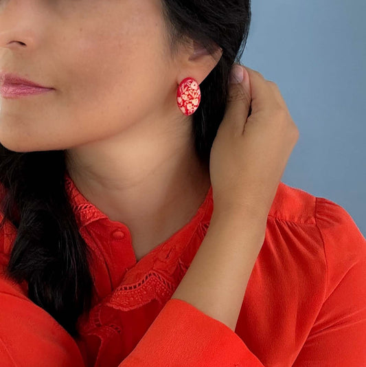 Woman wearing a red blouse and red earrings of tagua nuts, engraved with a floral pattern.