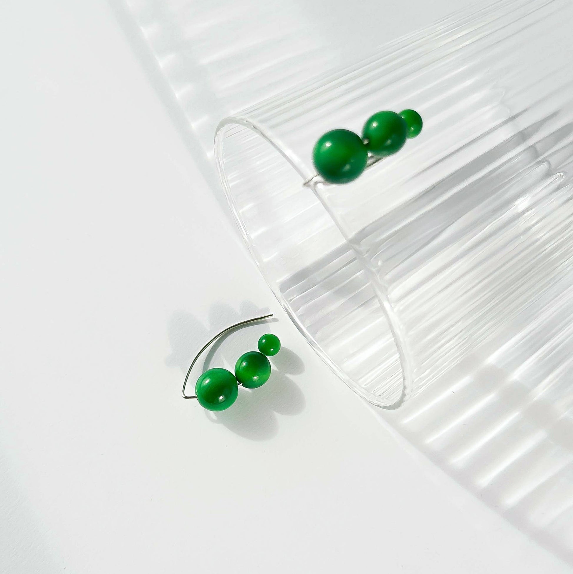 Green beaded hoop earrings displayed on a clear ribbed glass cylinder against a bright white background.