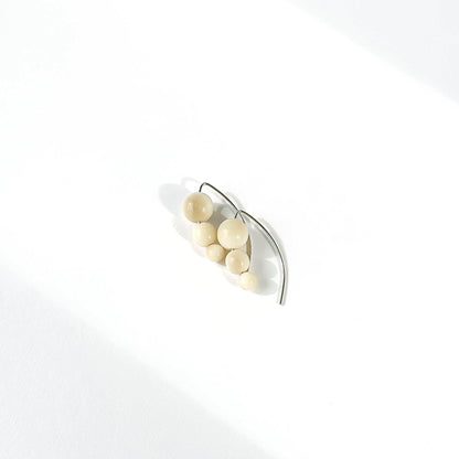 A pair of minimalist silver earrings featuring a cluster of small, matte cream-colored beads on a curved silver hook, photographed on a clean white surface with soft diagonal shadows.