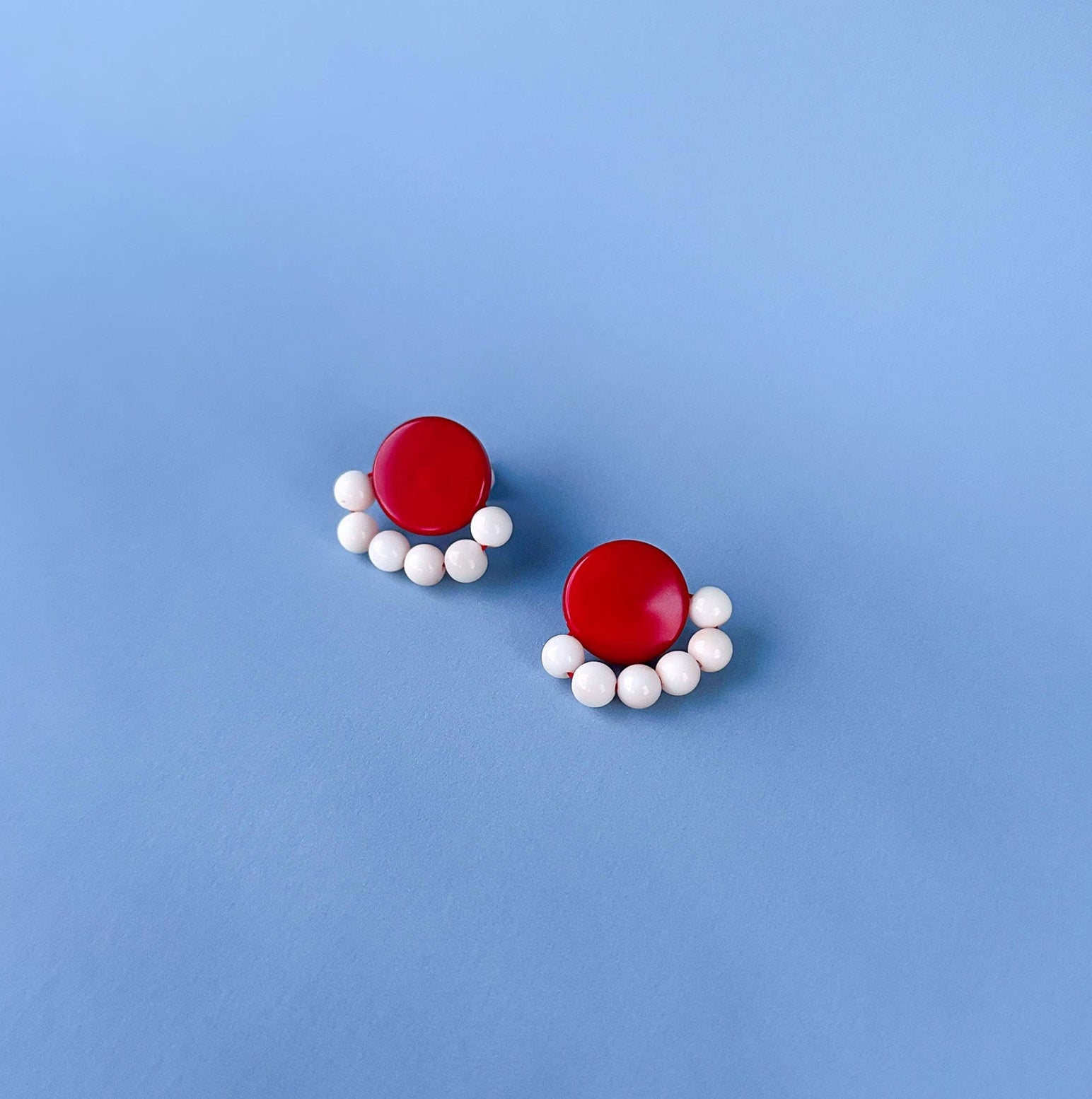 Pair of earrings with red and white tagua nut beads on a blue background