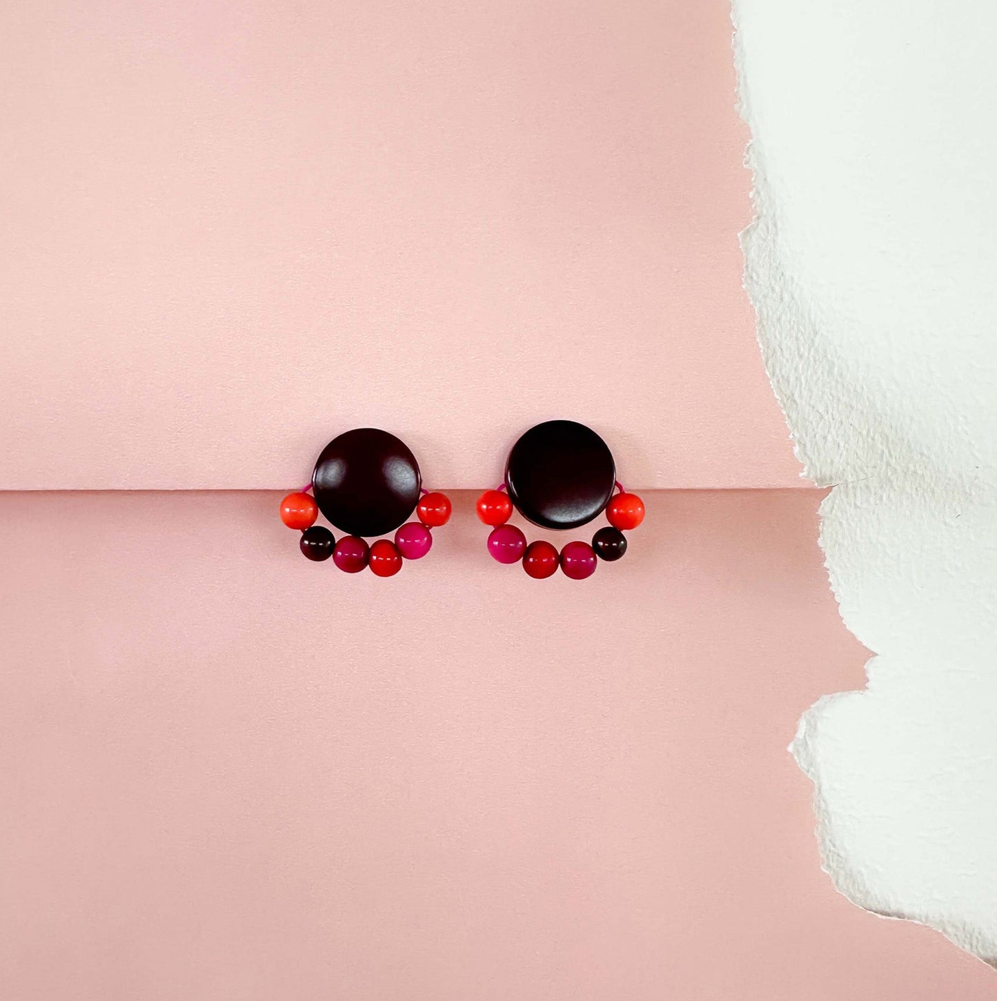 Pair of tagua nut earrings with black and red beads on a pink background