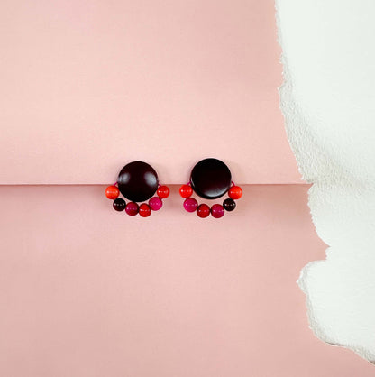 Pair of tagua nut earrings with black and red beads on a pink background