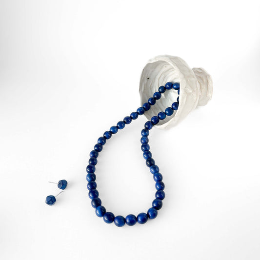 Blue tagua beaded necklace draped over a white vase on a white background