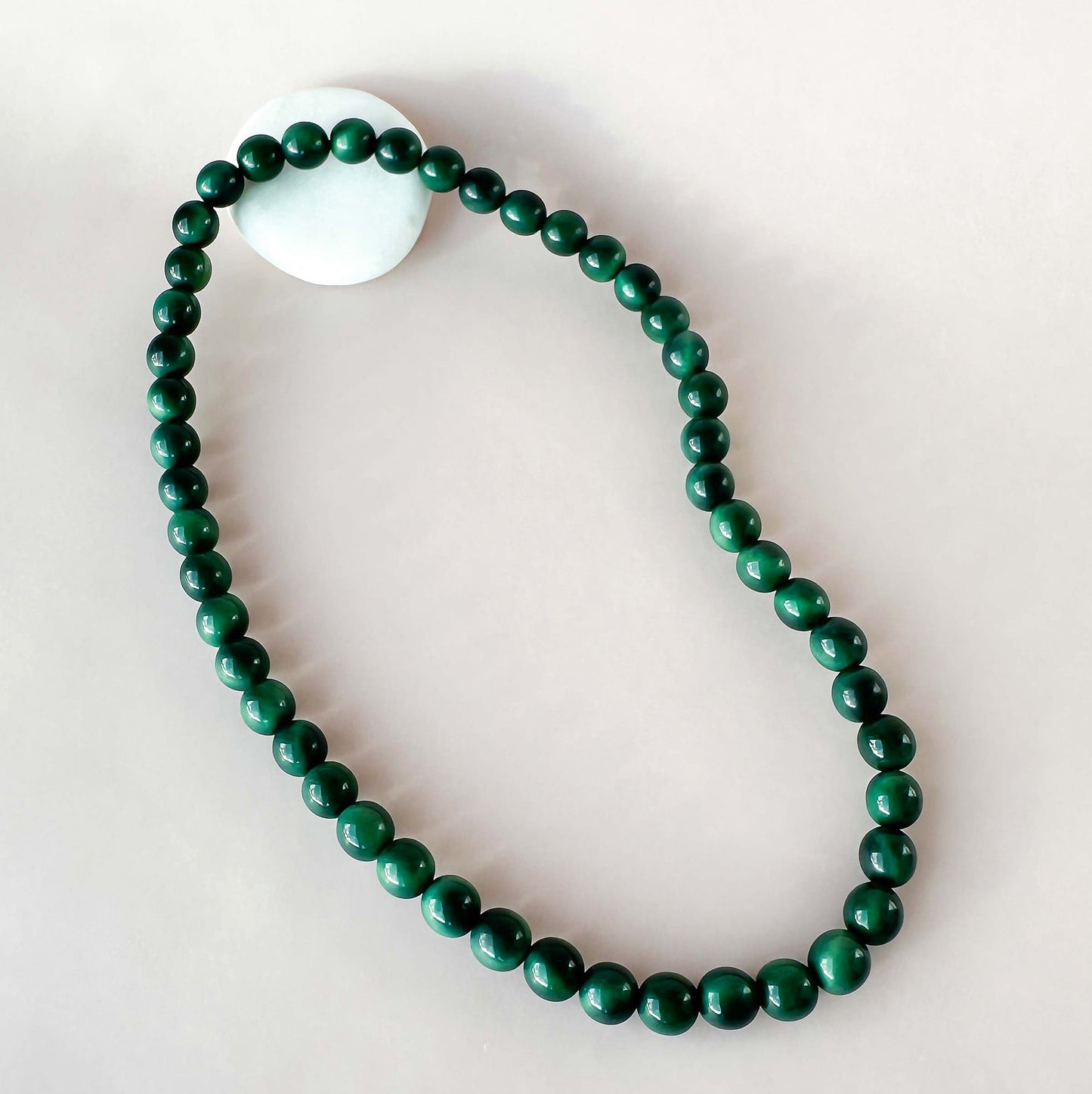 Green beaded tagua nut necklace with a white stone on a blue background