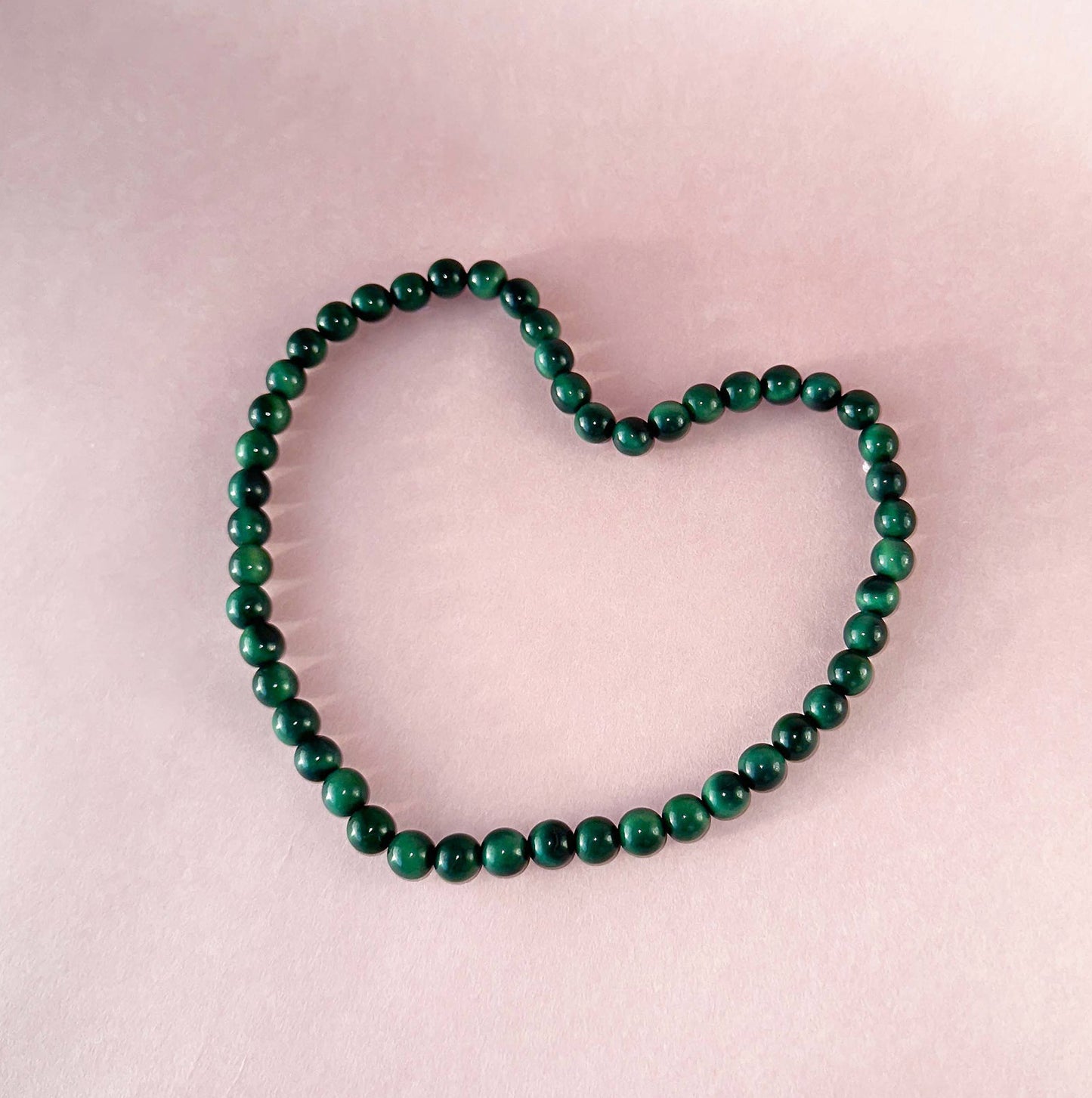 Green beaded tagua nut necklace shaped like a heart on a rose background