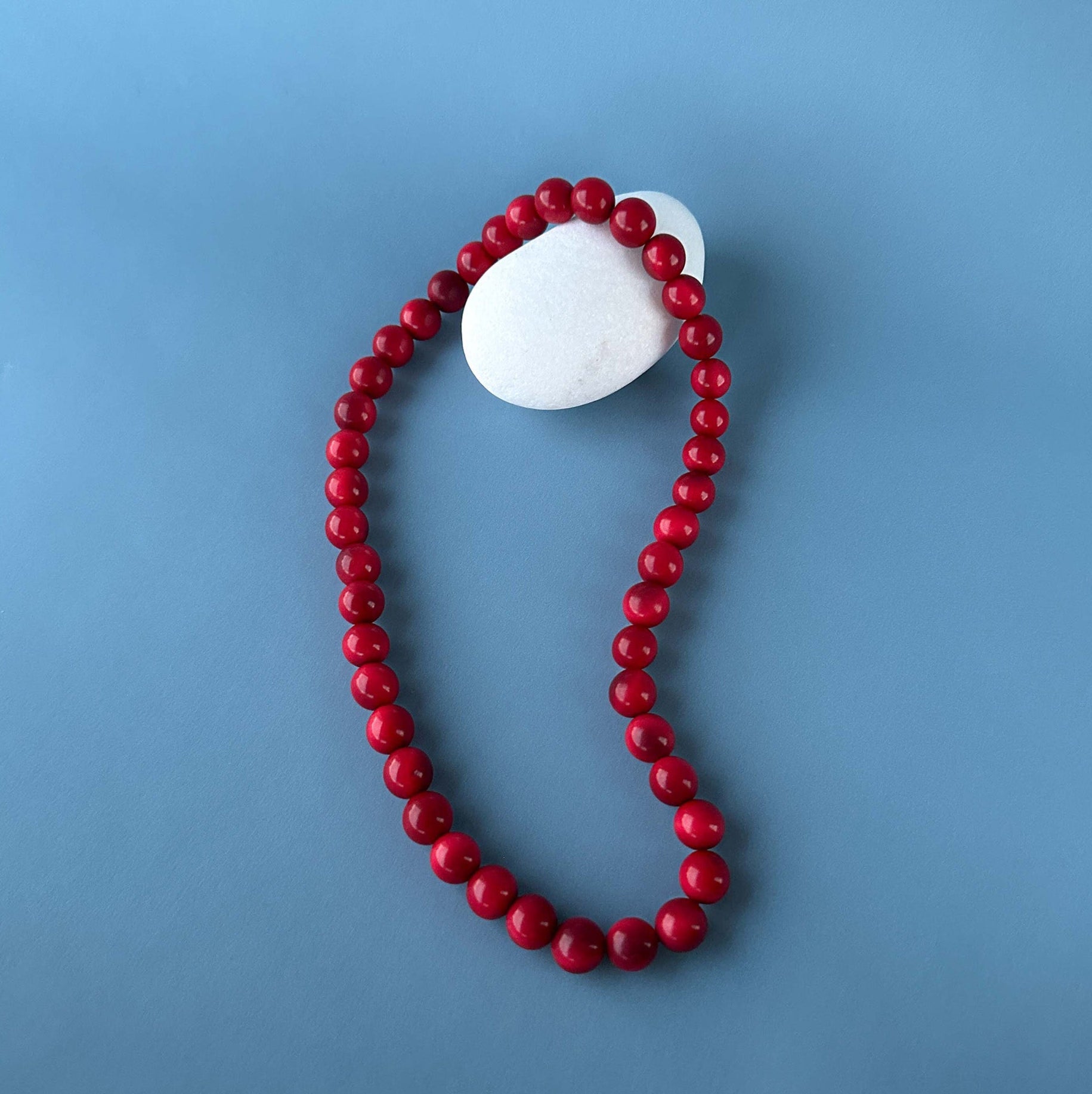 Red beaded tagua nut necklace with a white stone on a blue background